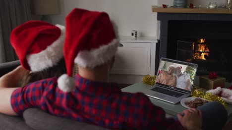 Happy-caucasian-couple-on-video-call-on-laptop-with-senior-couple-at-christmas-time