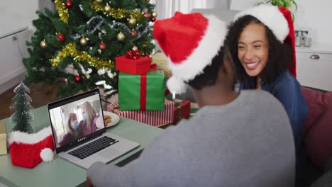 Happy-african-american-couple-on-video-call-with-female-friends-in-face-masks-at-christmas-time
