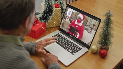 Happy-caucasian-senior-man-on-video-call-with-santa-claus-in-face-mask-at-christmas-time