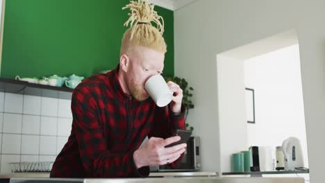 Nachdenklicher-Afroamerikanischer-Albino-Mann-Mit-Dreadlocks,-Der-Sein-Smartphone-Benutzt-Und-Kaffee-Trinkt