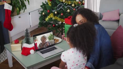 Happy-african-american-mother-and-daughter-on-video-call-with-grandmother-at-christmas-time