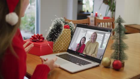 Happy-caucasian-woman-on-video-call-with-female-friend-and-daughter-at-christmas-time