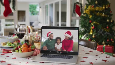 Glückliche-Afroamerikanische-Familie-Mit-Weihnachtsmützen-Auf-Laptop,-Der-Auf-Dem-Weihnachtstisch-Liegt