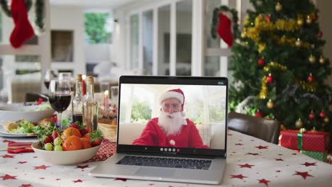 Glücklicher-Kaukasischer-Weihnachtsmann-Auf-Dem-Laptop,-Der-Auf-Dem-Weihnachtstisch-Liegt