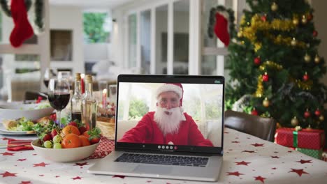 Happy-caucasian-santa-claus-on-laptop-lying-on-christmas-table