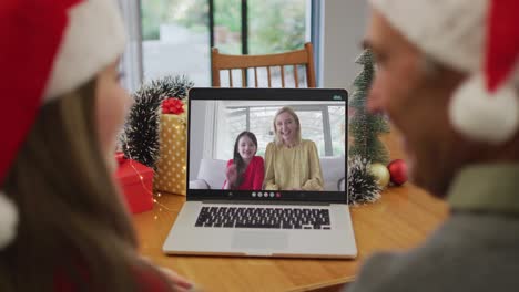 Happy-caucasian-senior-couple-on-video-call-with-female-friend-and-her-daughter-at-christmas-time