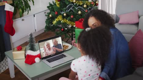 Happy-african-american-mother-and-daughter-on-video-call-on-laptop-with-senior-couple-at-christmas