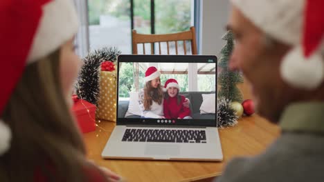 Rückansicht-Eines-Kaukasischen-Paares-Mit-Weihnachtsmützen,-Das-Während-Der-Weihnachtszeit-Einen-Videoanruf-Auf-Dem-Laptop-Führt