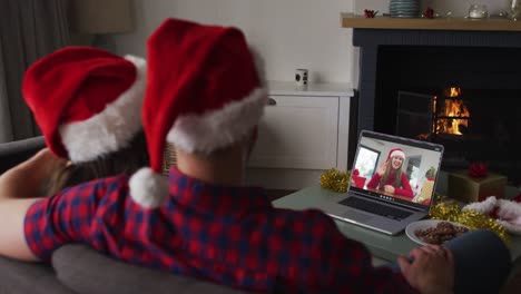 Happy-caucasian-couple-on-video-call-on-laptop-with-female-friend-at-christmas-time