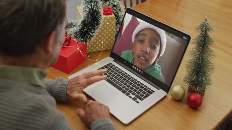 Happy-caucasian-senior-man-on-video-call-with-boy-in-santa-hat-at-christmas-time