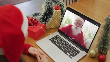 Caucasian-woman-on-video-call-on-laptop-with-santa-claus-at-christmas-time
