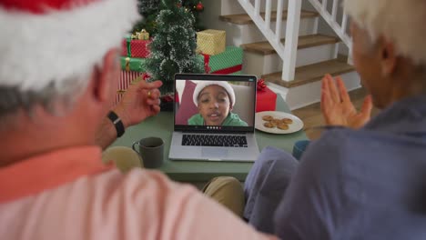 Happy-caucasian-senior-couple-on-video-call-on-laptop-with-boy-in-santa-hat-at-christmas-time