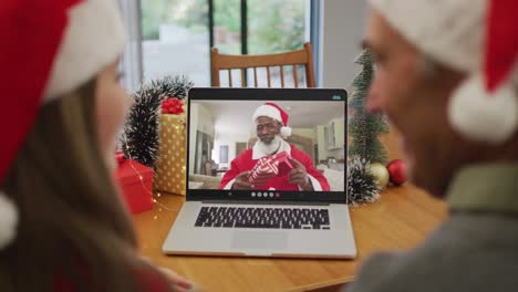 Caucasian-granddaughter-and-grandfather-on-video-call-with-santa-claus-at-christmas-time