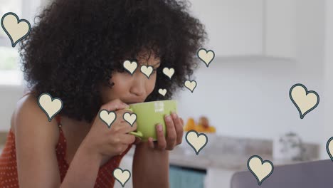 Animation-of-social-media-heart-icons-over-biracial-woman-drinking-coffee