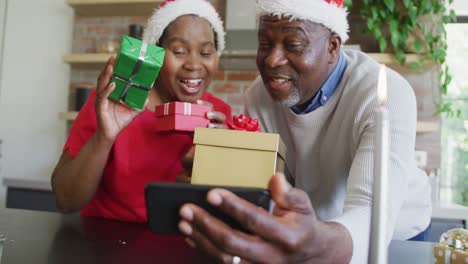 Feliz-Pareja-De-Ancianos-Afroamericanos-Con-Sombreros-De-Santa-En-Videollamada-En-Un-Teléfono-Inteligente-En-Navidad