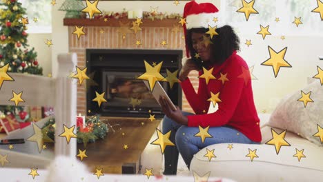 Gelbe-Sterne-Gegen-Eine-Afroamerikanische-Frau,-Die-Zu-Weihnachten-Einen-Videoanruf-Auf-Einem-Digitalen-Tablet-Führt