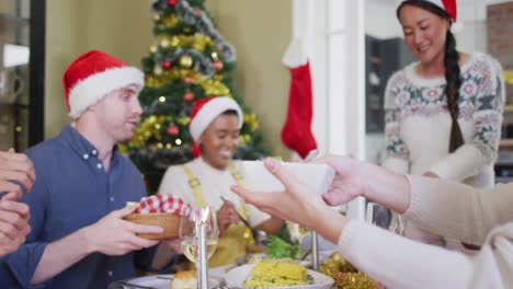 Fröhliche-Gruppe-Verschiedener-Freunde-In-Weihnachtsmützen,-Die-Das-Essen-Zur-Weihnachtszeit-Feiern