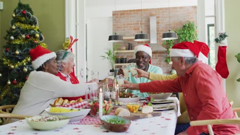 Fröhliche-Gruppe-Verschiedener-älterer-Freunde,-Die-Zur-Weihnachtszeit-Essen-Feiern-Und-Saft-Trinken