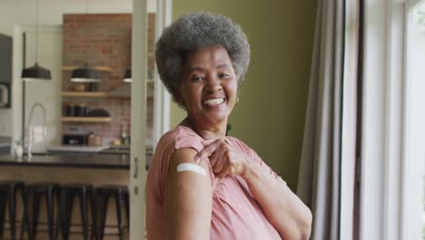 Happy-african-american-senior-woman-showing-plaster-on-arm-after-covid-vaccination