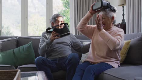 Happy-mixed-race-senior-couple-wearing-vr-headset-and-having-fun-at-home