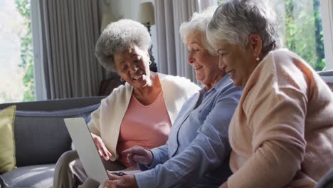 Three-diverse-senior-women-using-laptop-together-sitting-on-the-couch-at-at-home