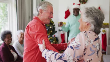 Glückliches-Kaukasisches-älteres-Paar,-Das-Zur-Weihnachtszeit-Zusammen-Mit-Freunden-Im-Hintergrund-Tanzt