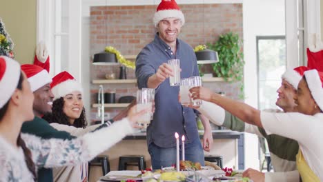 Happy-group-of-diverse-friends-in-santa-hats-celebrating-meal,-toasting-with-juice-at-christmas-time
