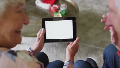 Caucasian-senior-couple-in-santa-hats-on-video-call-on-tablet-with-copy-space-at-christmas-time
