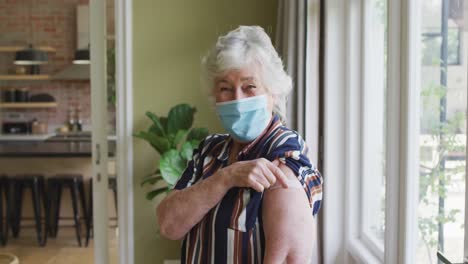 Caucasian-senior-woman-wearing-face-mask-showing-her-vaccinated-shoulder-at-home