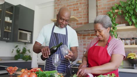 Glückliches-Afroamerikanisches-Seniorenpaar,-Das-Zusammen-Kocht-Und-In-Der-Küche-Wein-Trinkt