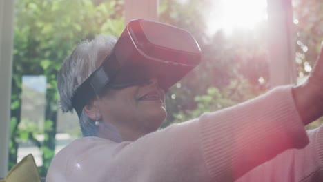 Happy-mixed-race-senior-woman-wearing-vr-headset-and-having-fun-at-home
