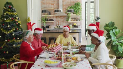 Grupo-De-Amigos-Mayores-Felices-Y-Diversos-Con-Sombreros-De-Papá-Noel-Comiendo-Juntos-La-Cena-De-Navidad-En-Casa