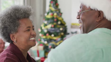Glückliches-Afroamerikanisches-Seniorenpaar,-Das-Zur-Weihnachtszeit-Zusammen-Mit-Freunden-Im-Hintergrund-Tanzt