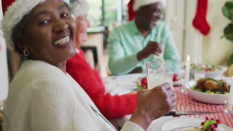 Happy-african-american-senior-woman-celebrating-meal-with-friends-at-christmas-time