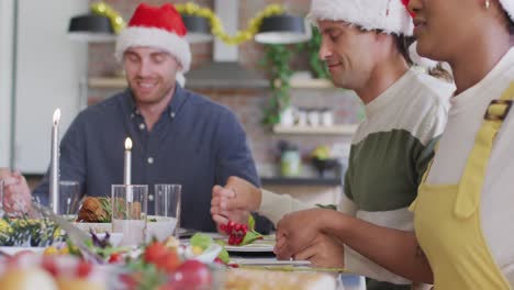 Feliz-Grupo-De-Amigos-Diversos-Con-Gorros-De-Papá-Noel-Celebrando-La-Comida-En-Navidad