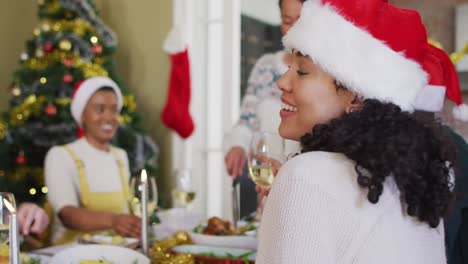 Fröhliche-Frau-Mit-Gemischter-Abstammung-Und-Weihnachtsmütze-Feiert-Das-Essen-Mit-Freunden-Zur-Weihnachtszeit