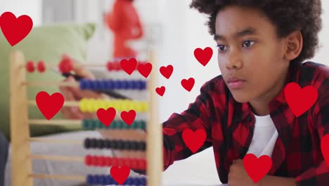 Animation-of-social-media-heart-icons-over-smiling-biracial-boy-using-abacus