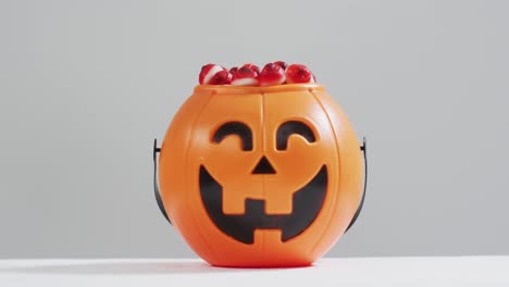 Scary-halloween-pumpkin-printed-bucket-full-of-candies-against-grey-background