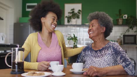 Happy-african-american-adult-daughter-and-senior-mother-embracing-and-drinking-coffee,-slow-motion