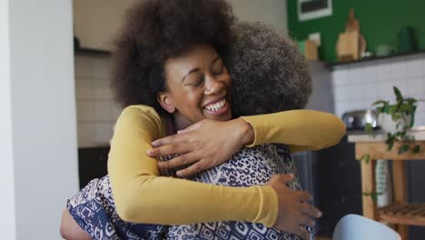 Happy-african-american-adult-daughter-and-senior-mother-hugging-in-kitchen-at-home,-slow-motion