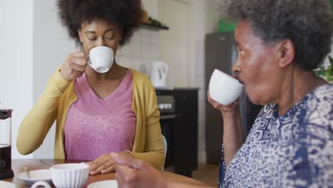 Happy-african-american-adult-daughter-and-senior-mother-drinking-coffee,-slow-motion