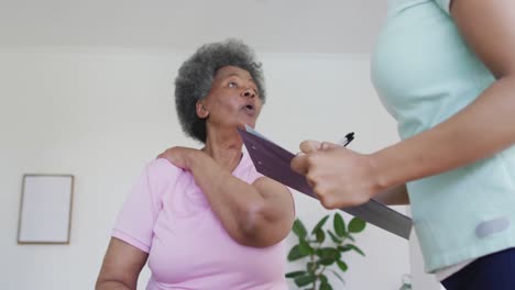 Afroamerikanische-Physiotherapeutin-Mit-Gesichtsmaske-Hilft-älteren-Patientinnen-Beim-Training