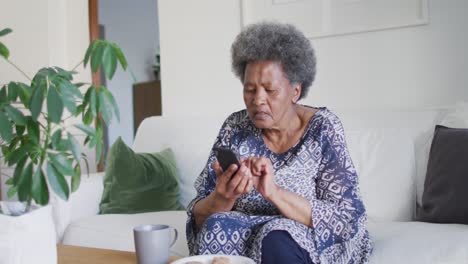 Afroamerikanische-ältere-Frau,-Die-Auf-Der-Couch-Sitzt-Und-Ihr-Smartphone-Benutzt