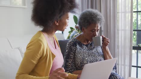 Happy-african-american-adult-daughter-and-senior-mother-using-laptop-at-home,-slow-motion