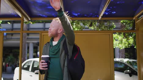 Happy-albino-african-american-man-with-dreadlocks-holding-takeaway-coffee-and-waving