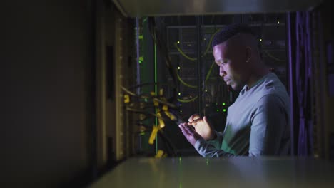 African-american-male-computer-technician-using-smartphone-working-in-business-server-room
