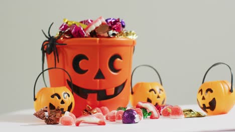 Gruseliger-Halloween-Kürbis-Bedruckter-Eimer-Voller-Süßigkeiten-Vor-Grauem-Hintergrund