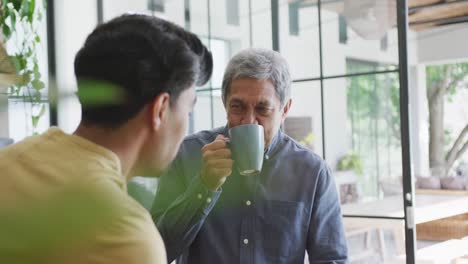 Man-sipping-coffee-from-mug-while-listening-to-son's-conversation-in-kitchen-at-home