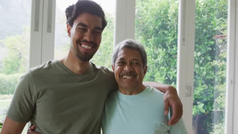 Portrait-of-cheerful-biracial-young-man-with-hand-on-shoulder-of-father-at-home