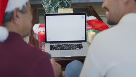 Happy-son-and-father-making-christmas-video-call-on-laptop-with-blank-white-screen-and-copy-space